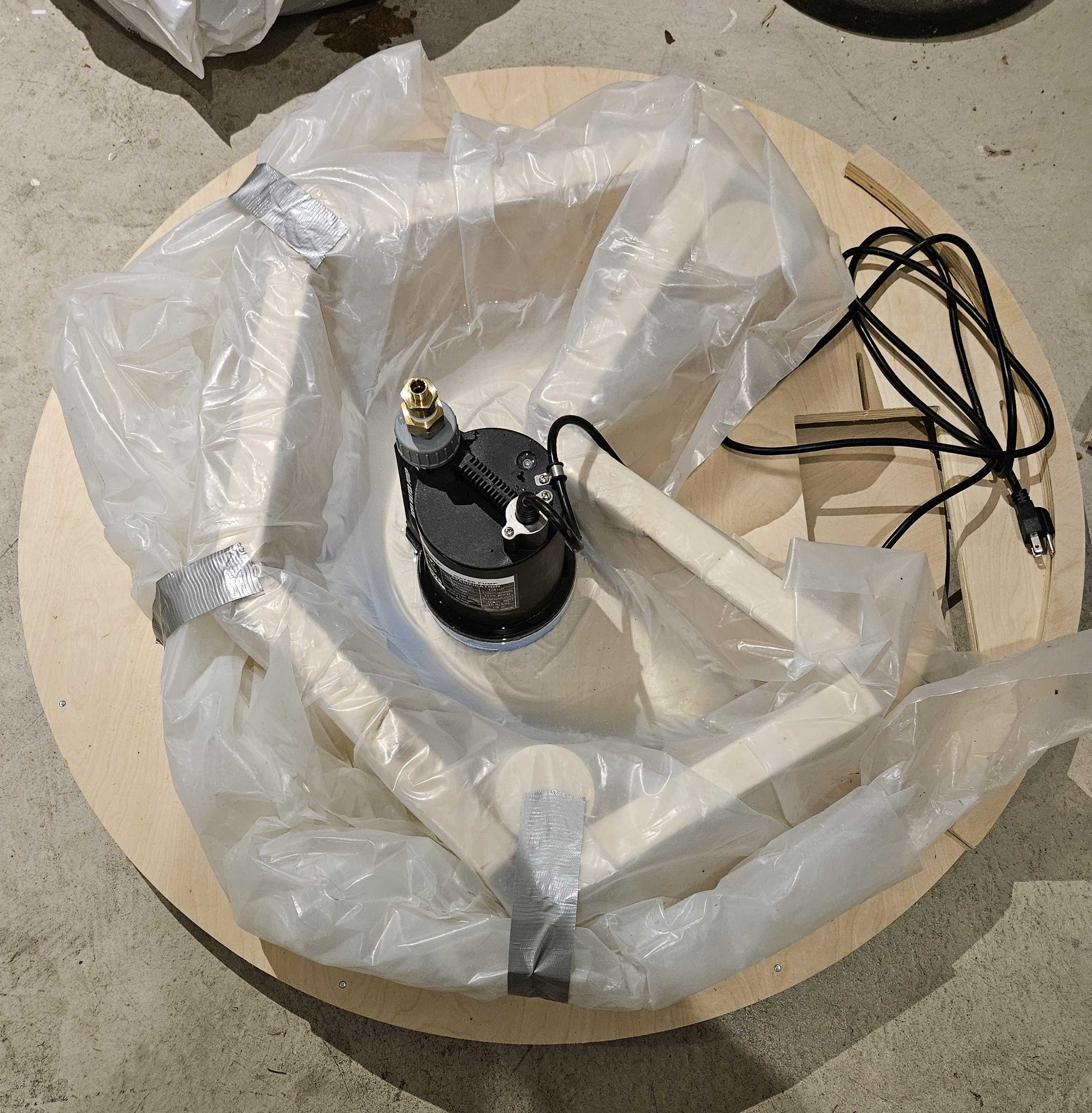 A water pump sitting on top of a plastic tarp propped up with wooden blocks, which serves as the Orbital Flush water tank.