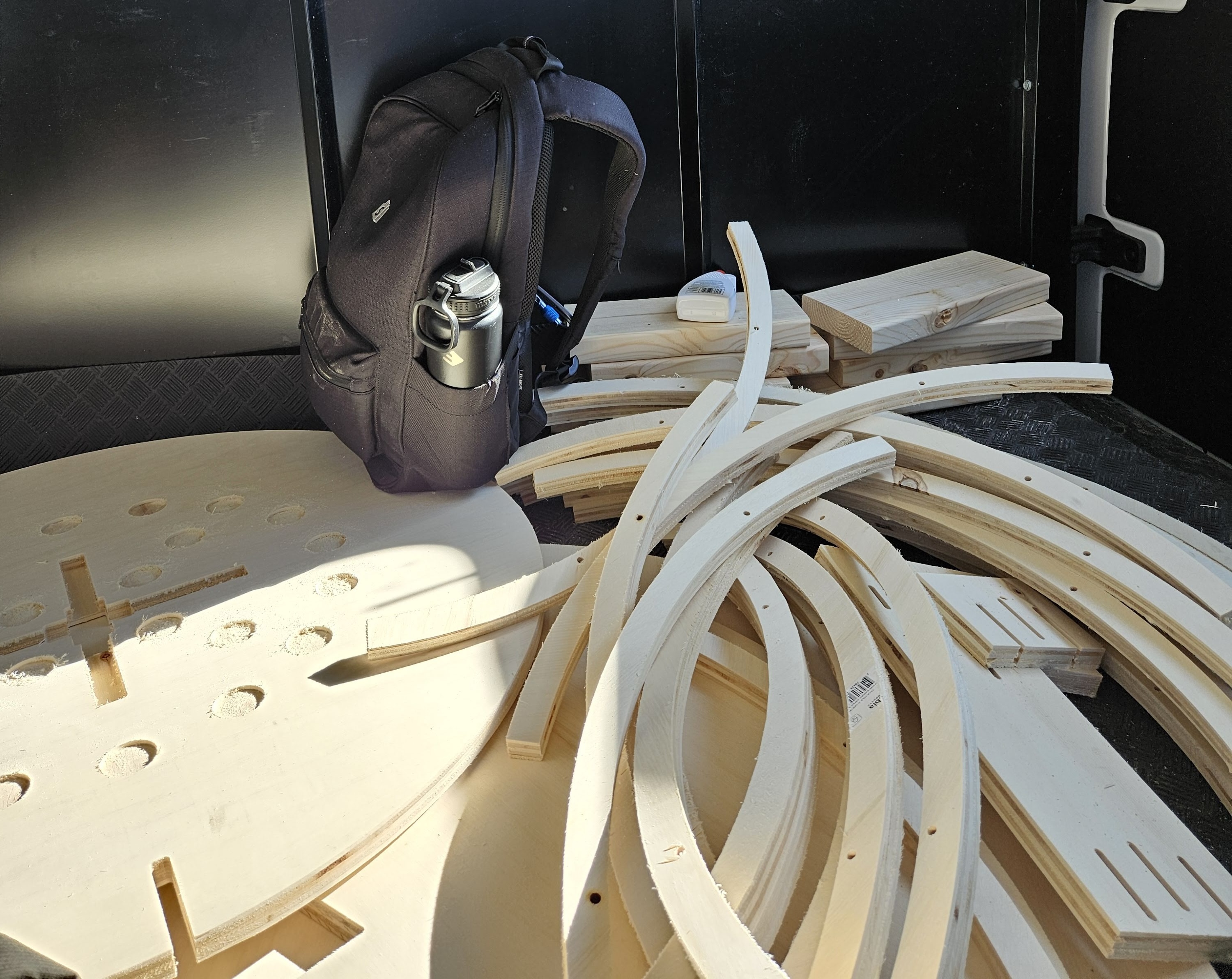 A collection of unassembled wooden pieces comprising Orbital Flush, piled haphazardly on the inside of our UHaul.